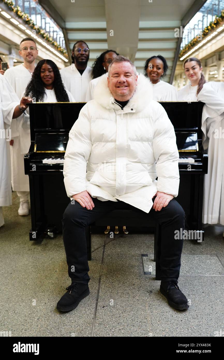 L'ex cantante degli East 17 Tony Mortimer sorprende i pendolari della stazione St Pancras International di Londra con una performance pop-up del suo numero uno natalizio 1994 "Stay Another Day", supportato dal London Community Gospel Choir. La performance arriva quando Tony ha collaborato con l'associazione benefica Nordoff e Robbins per celebrare il 30° anniversario dell'uscita della canzone. Data foto: Venerdì 13 dicembre 2024. Foto Stock