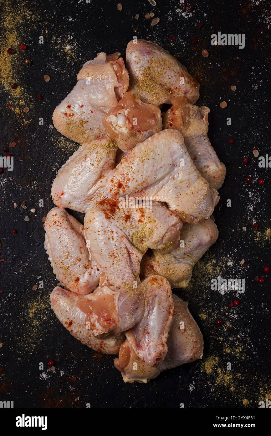 Ali di pollo crude fresche, con spezie, su sfondo nero Foto Stock