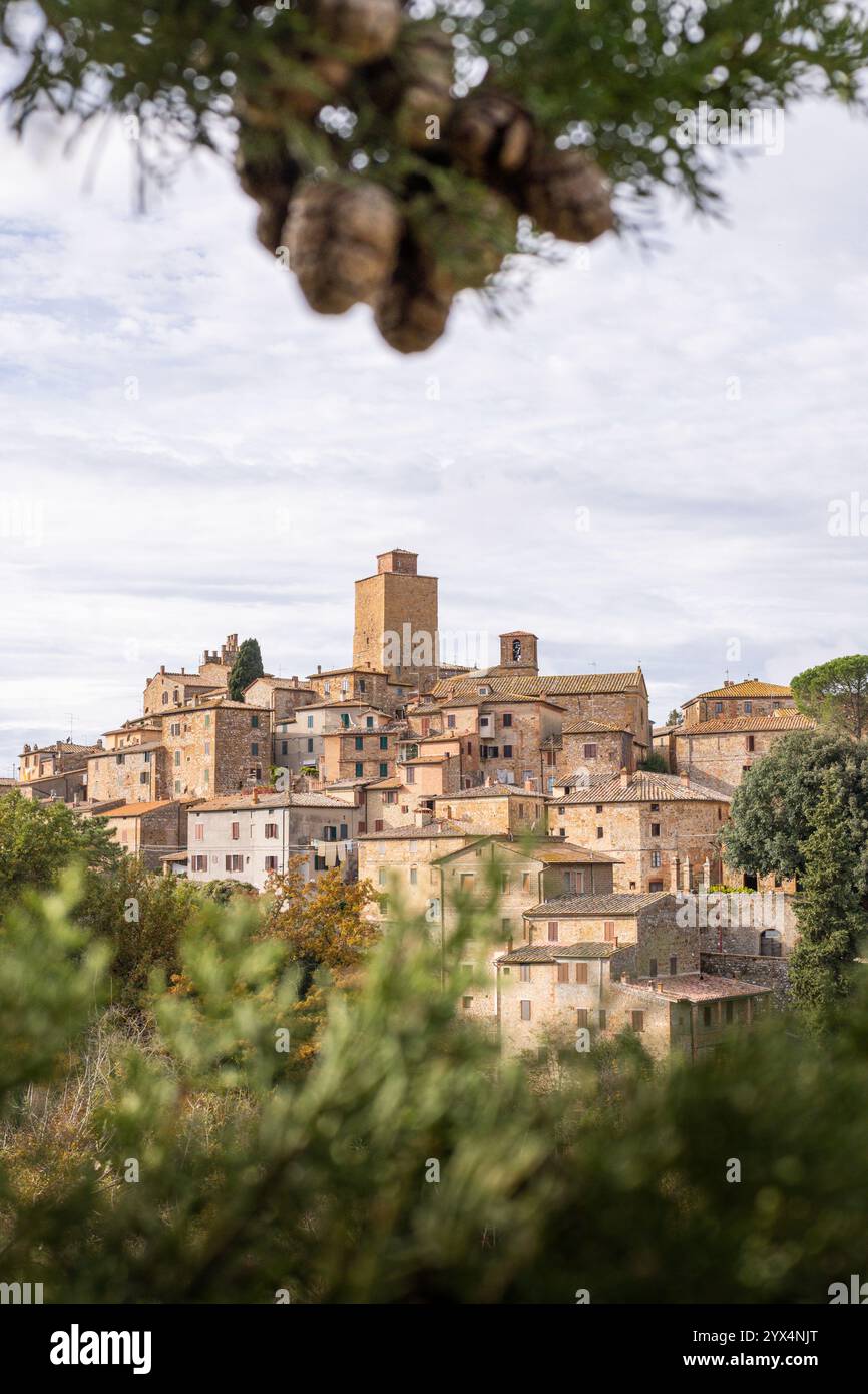 Vista da cartolina del villaggio collinare di Petroio attraverso i rami di cipressi in Toscana, Italia. Orientamento verticale Foto Stock