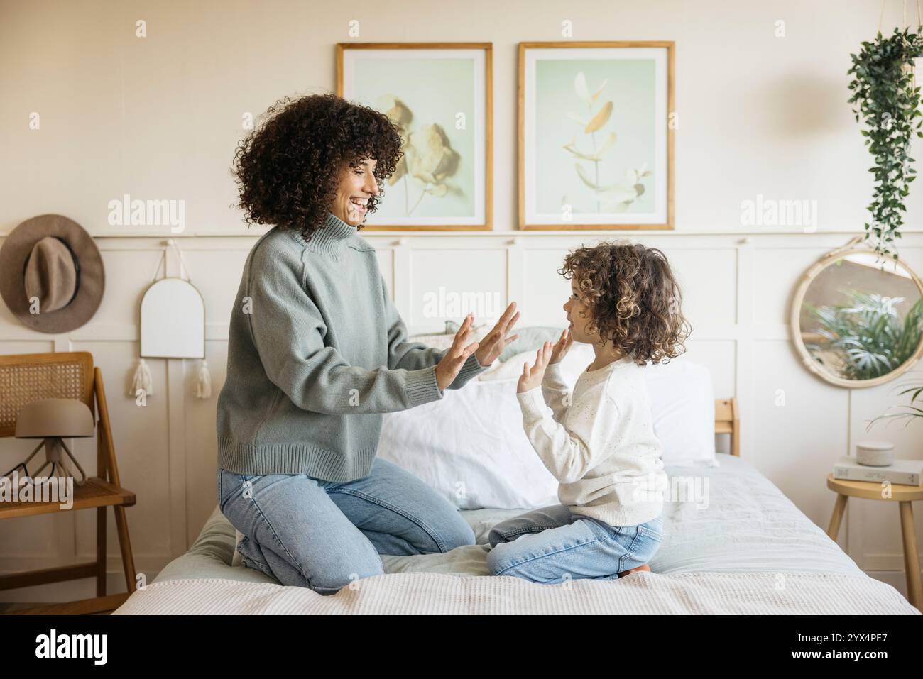 Una scena gioiosa di madre e bambino che giocano insieme su un letto in un'accogliente camera da letto, con un legame familiare e un caldo. Foto Stock