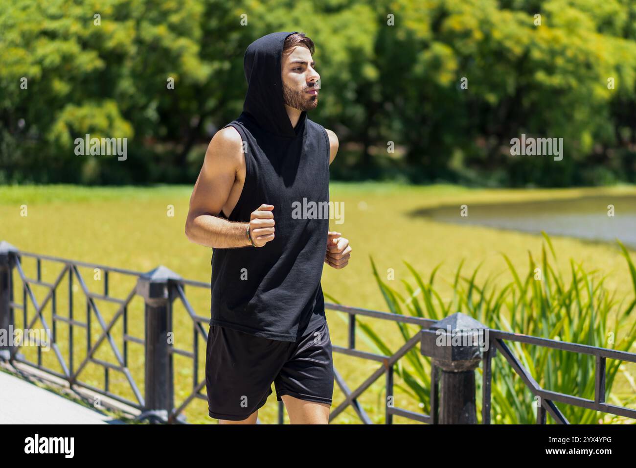 Un giovane motivato si muove con sicurezza mentre fa jogging lungo un sentiero sul lago nel parco. Foto Stock