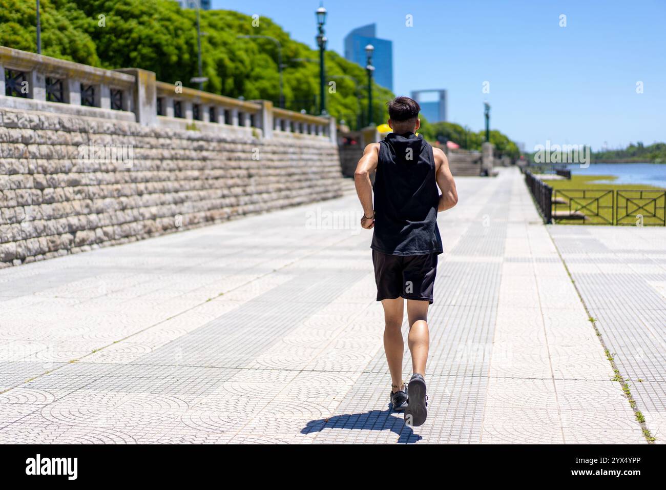 Giovane uomo in forma che fa jogging attraverso i vivaci sentieri di un parco cittadino. Foto Stock