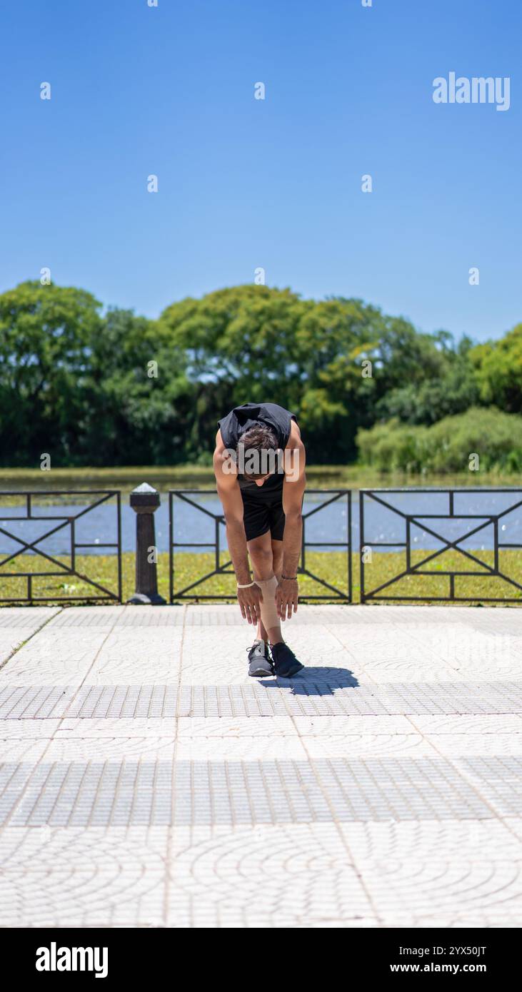 Allenati con un giovane che si allunga dopo l'allenamento vicino a un lago tranquillo nel parco cittadino. Foto Stock