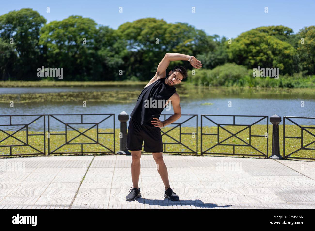 Routine di stretching post-esercizio per un giovane in forma vicino al lago nel parco cittadino. Foto Stock
