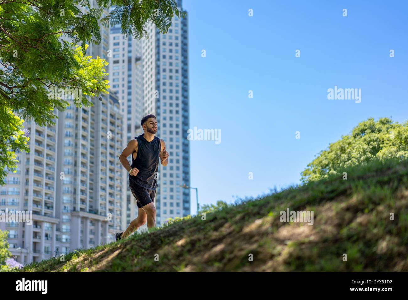Adatta il giovane ad una corsa dinamica attraverso un parco collinare dall'architettura moderna. Foto Stock