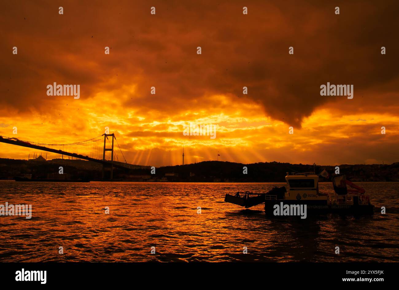 La barca per la pulizia del comune di Istanbul pulisce il mare nel Bosforo. Vista del Ponte dei Martiri del 15 luglio e della Moschea di Camlıca all'alba. Foto Stock