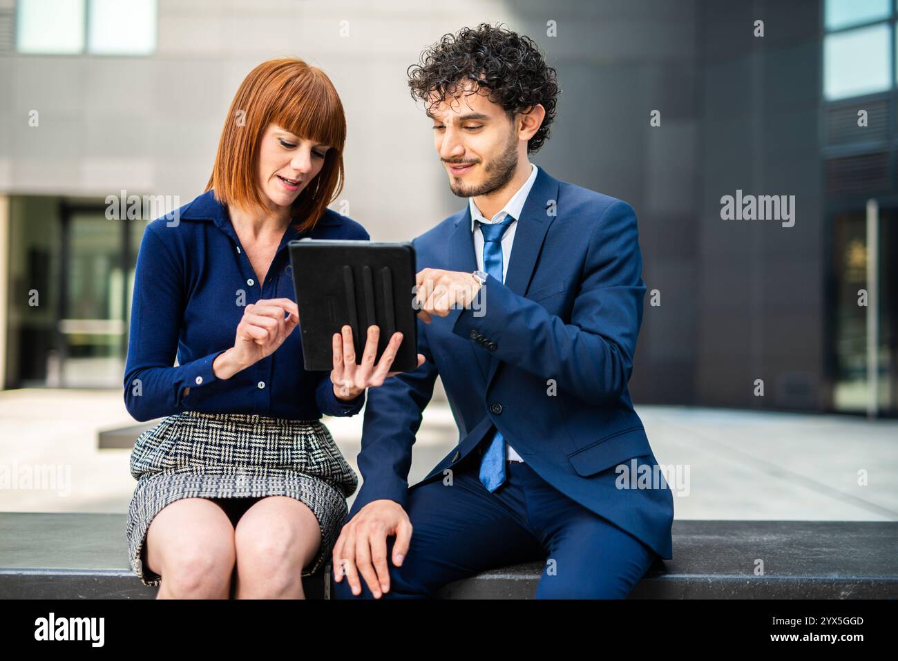Gli uomini d'affari si incontrano fuori, usando un tablet per una discussione di progetto in una città moderna. Vestite professionalmente, presentano lavoro di squadra e comunicazione Foto Stock