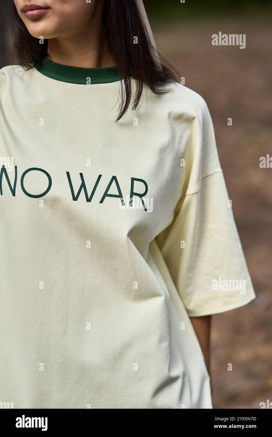 Individuo in cima alla guerra, prospettiva ravvicinata, testo verde, messaggio di pace, esterno, abbigliamento casual, espressione anti-guerra, in mezzo alla natura, anti-guerra st Foto Stock