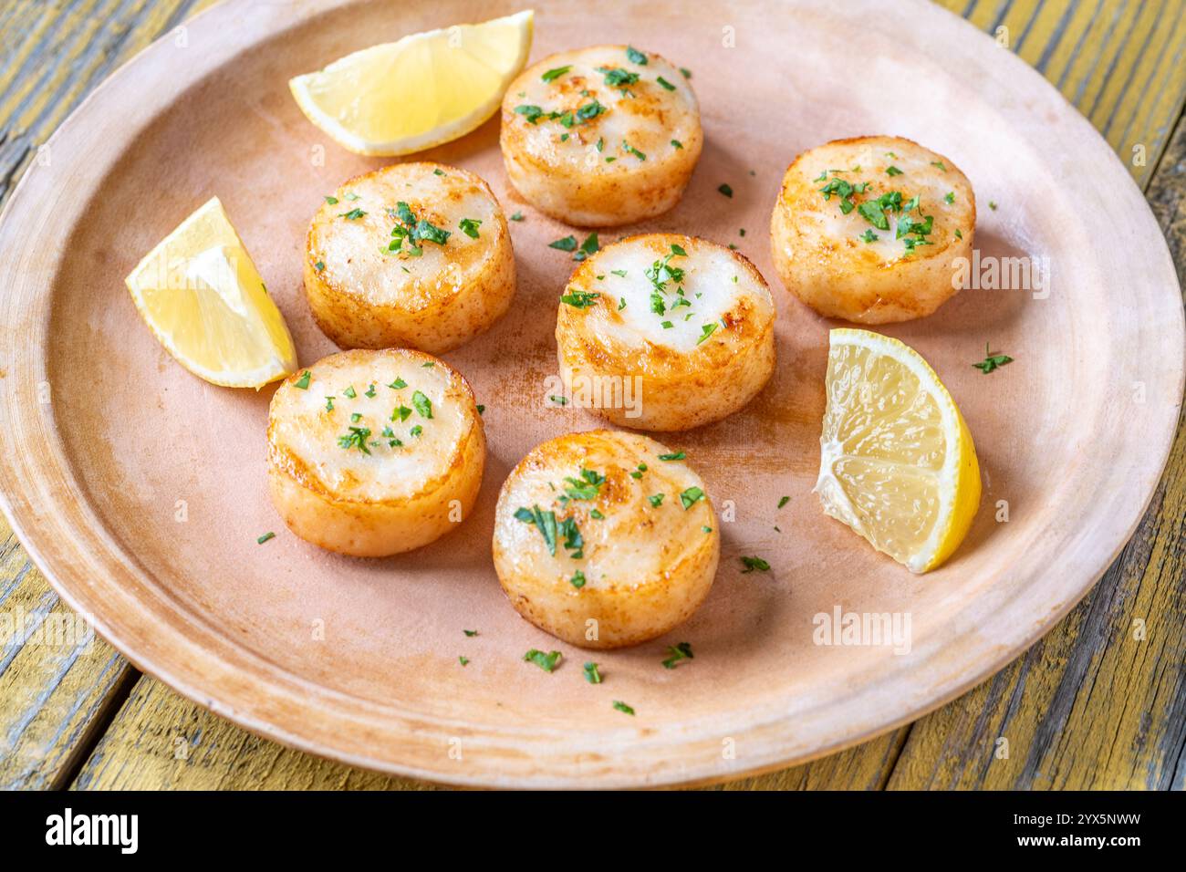 Morbide capesante fritte in burro servite con limone, prezzemolo, rustico fondo giallo Foto Stock