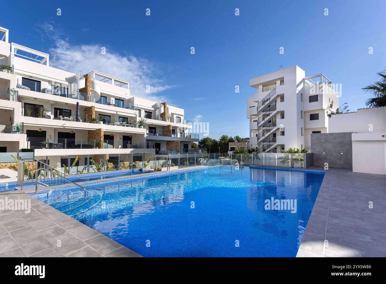 Un lussuoso complesso residenziale caratterizzato da una piscina incontaminata, balconi in vetro, architettura elegante e soleggiate aree di svago all'aperto. Foto Stock