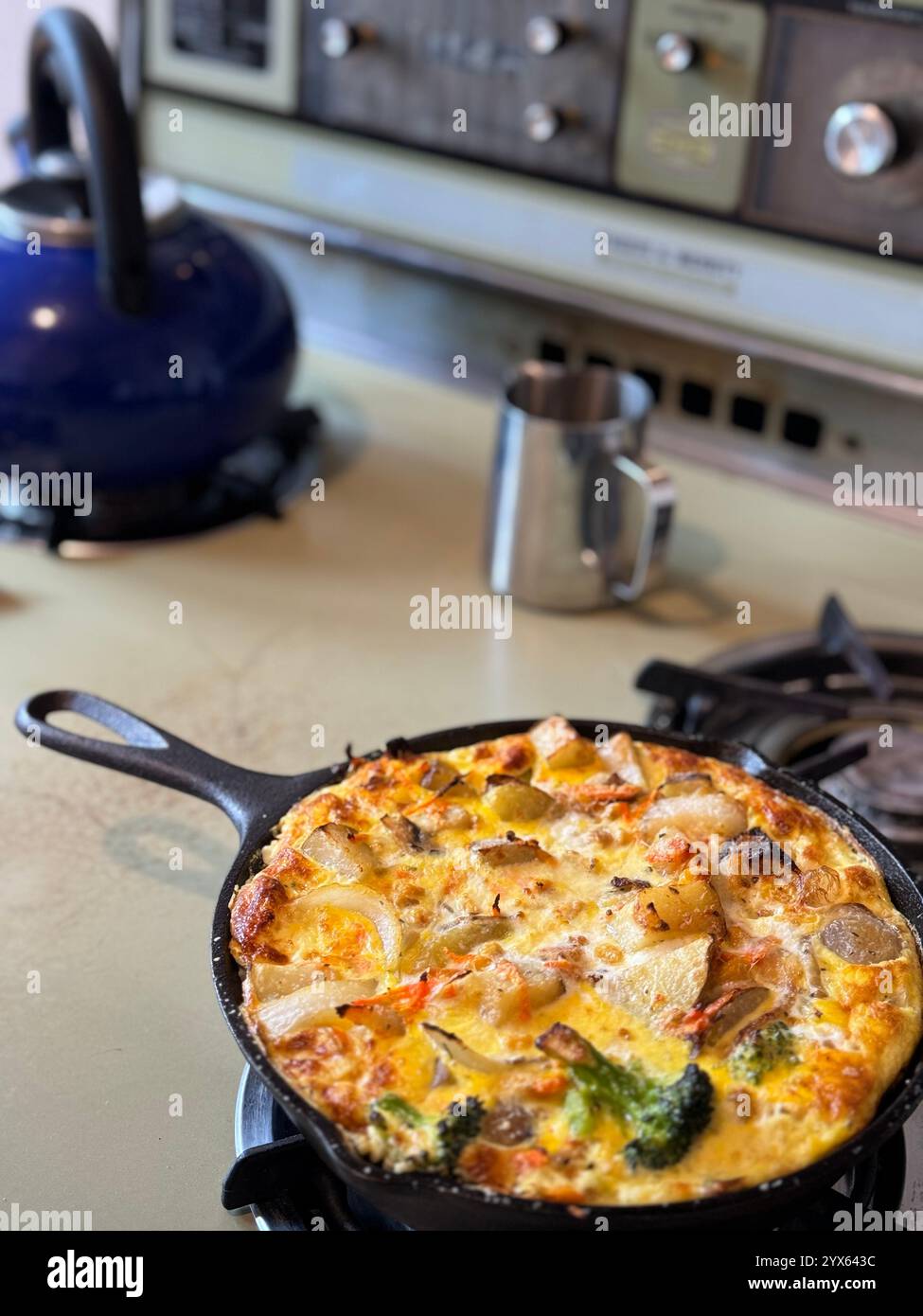Una sorta di frittata fatta di uova, patate, broccoli, cipolla e formaggio. Cotto in una padella in ghisa in una stufa vintage anni '1970. - Immagine stock catturata con smartphone