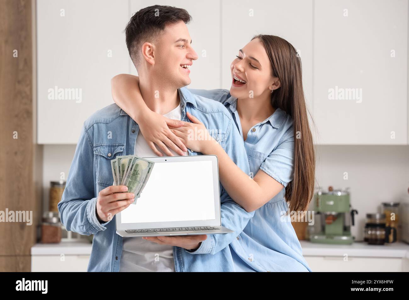 Felice giovane coppia con i soldi e un portatile vuoto in cucina Foto Stock