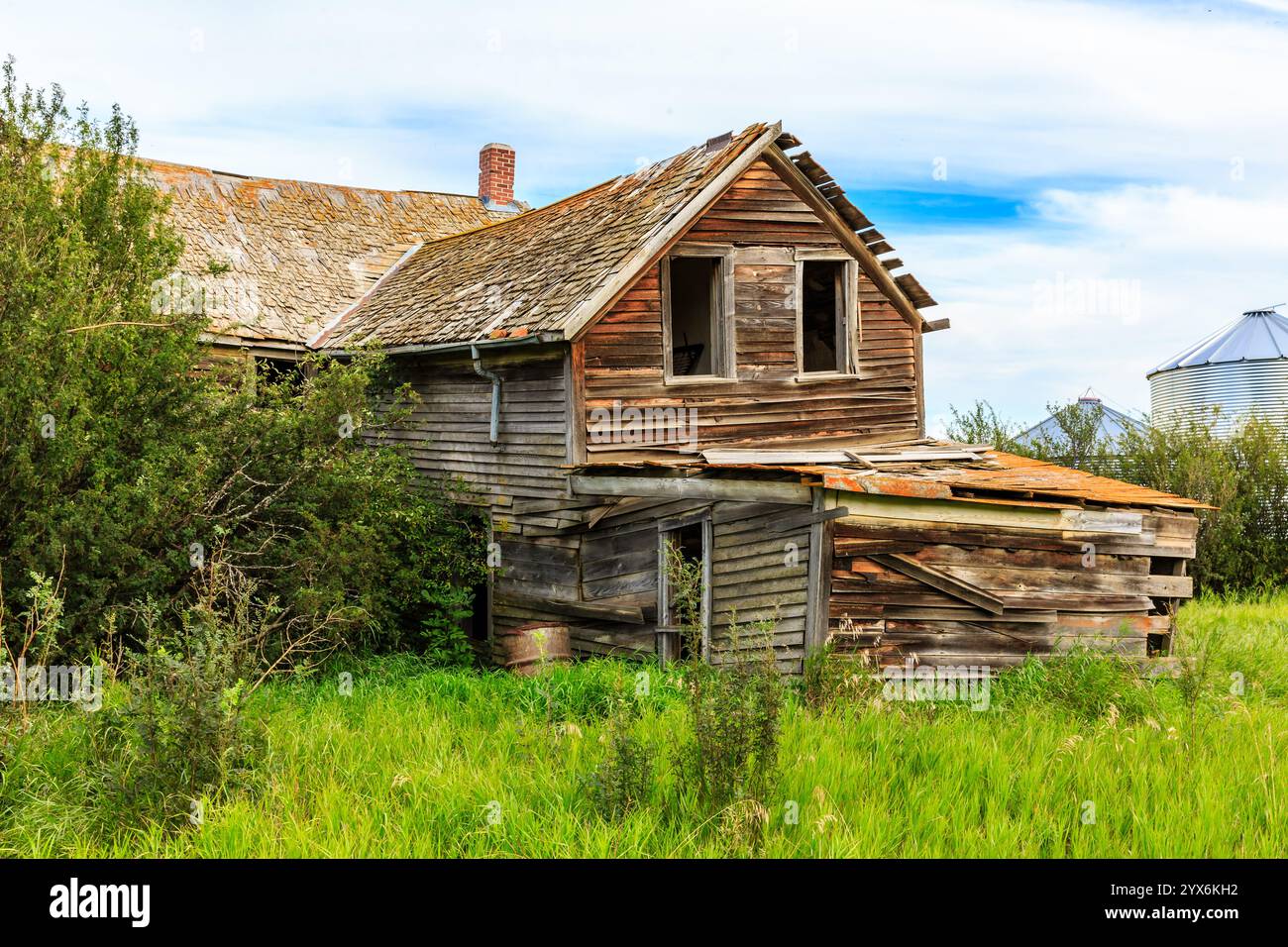Una vecchia casa fatiscente con un grande camino. La casa è circondata da un grande campo erboso Foto Stock