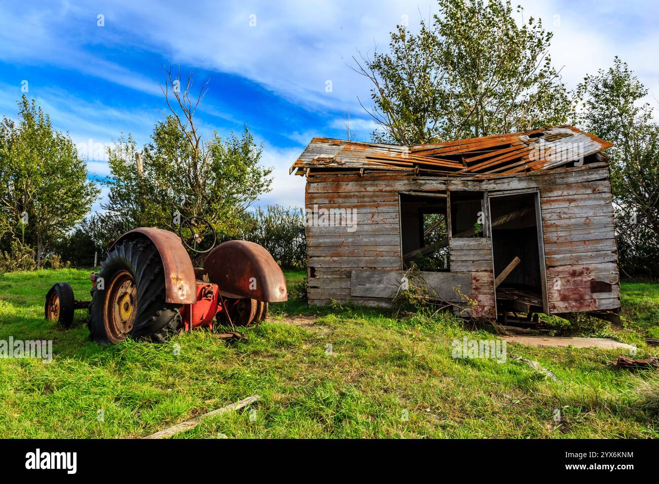 Un vecchio casale in rovina si trova in un campo erboso, con un trattore rosso arrugginito parcheggiato di fronte. La casa sembra essere in uno stato di disrepa Foto Stock