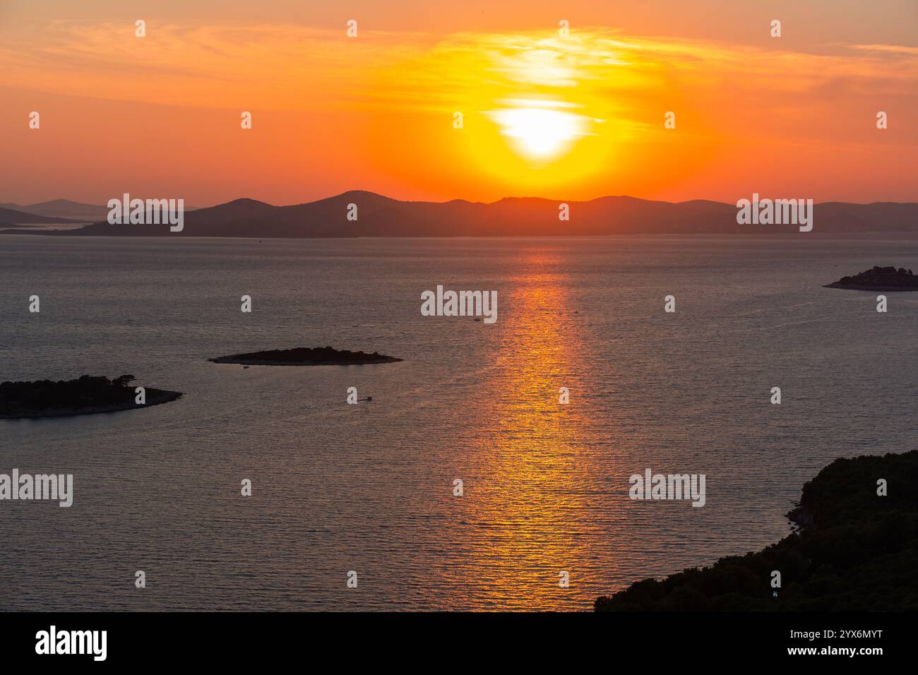 Tramonto dorato sul mare calmo con riflessi luminosi e sagome di piccole isole e colline lontane. Concetto di natura tranquilla, romantico paesaggio marino Foto Stock