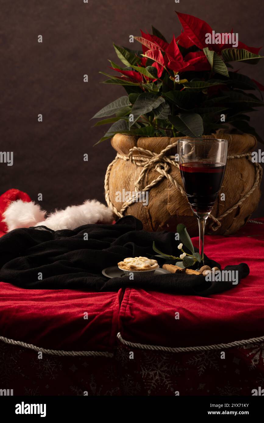 Una tavola festosa che include un bicchiere di VIN brulé con cinamone, una ricca scena con un cappello di babbo natale scartato e un piatto di torte tritate. Foto Stock