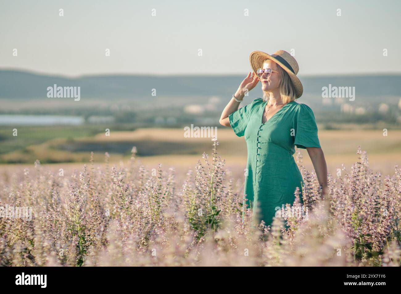 Campo di abbigliamento donna: Servizio fotografico estivo alla moda; la donna bionda in abito verde acqua si gode una giornata di sole in un campo di lavanda. Foto Stock