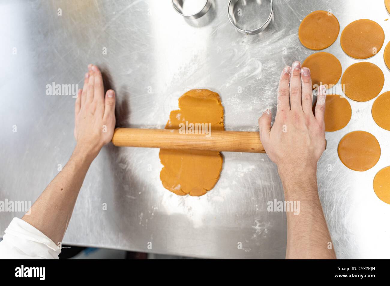 Le mani del fornaio stenderanno l'impasto sul tavolo di produzione con un mattarello. Il processo di preparazione dei biscotti in un forno o in un'officina. V Foto Stock