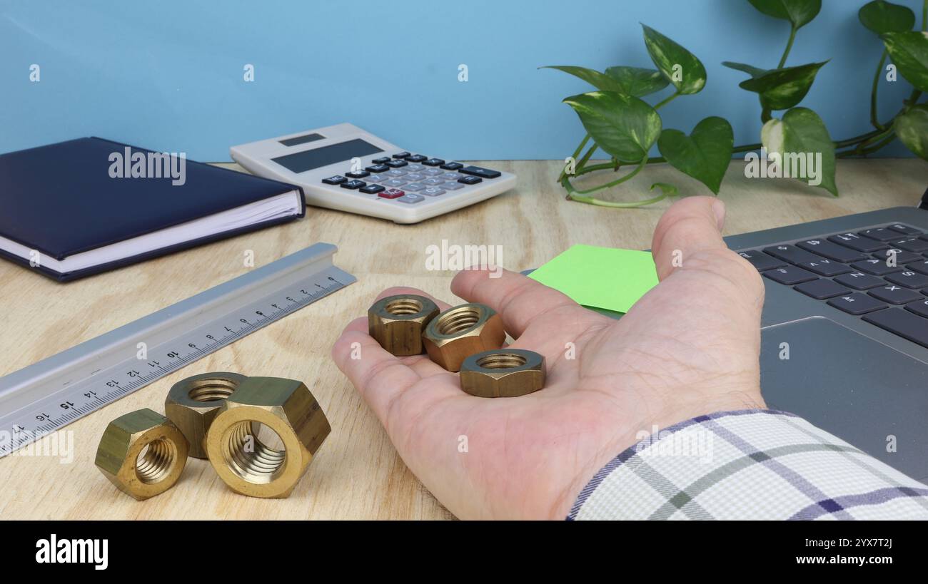 Man Hand mostra un gruppo di bulloni in ottone sulla scrivania con un computer e un righello lavoro di meccanico nell'ufficio. Foto Stock