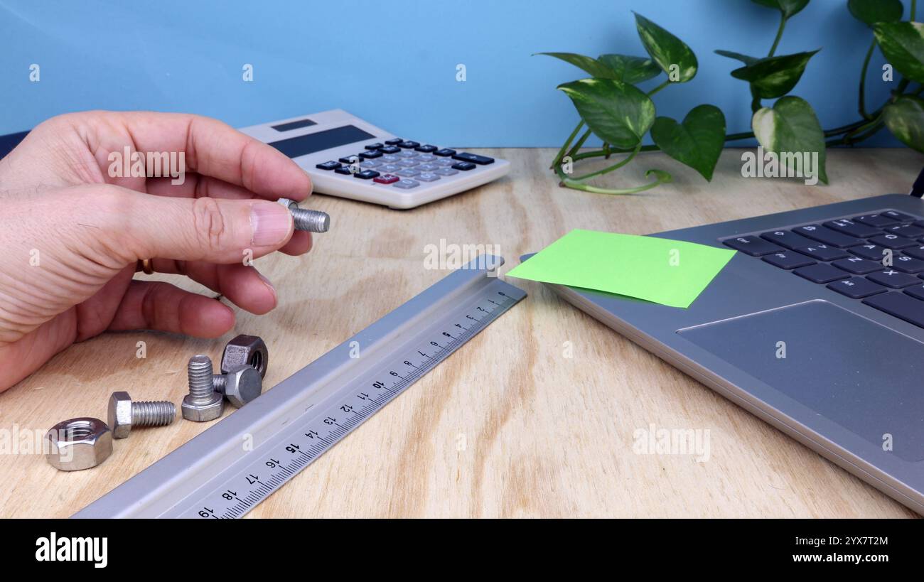 Man Hand mostra un gruppo di viti sulla scrivania con computer e righello in officina meccanica. Foto Stock