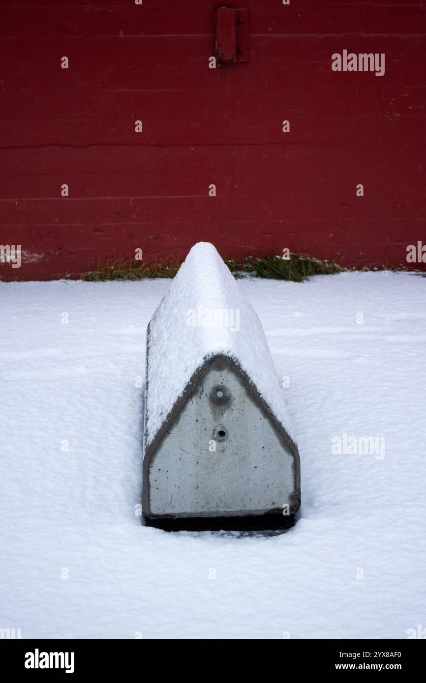 Oggetto a forma di casa con tetto tradizionale, per evitare l'ingresso di auto. Neve fresca. Muro rosso sullo sfondo. Porto di Narvik, Norvegia. Foto Stock