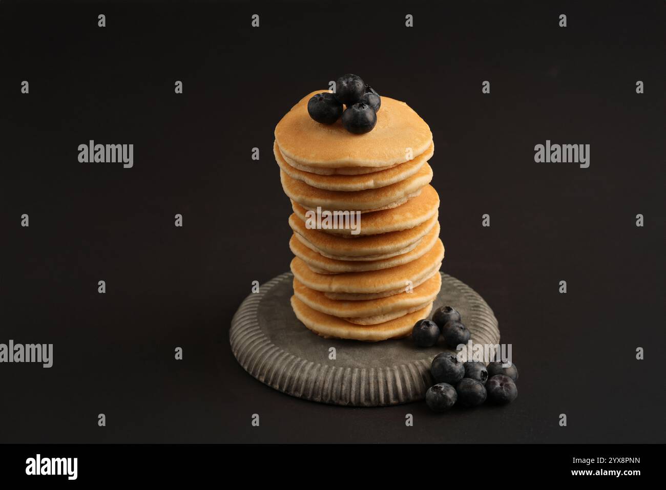 Immagine dello studio su sfondo nero di una pila di pancake su un piatto in peltro sormontato da mirtilli maturi. Foto Stock