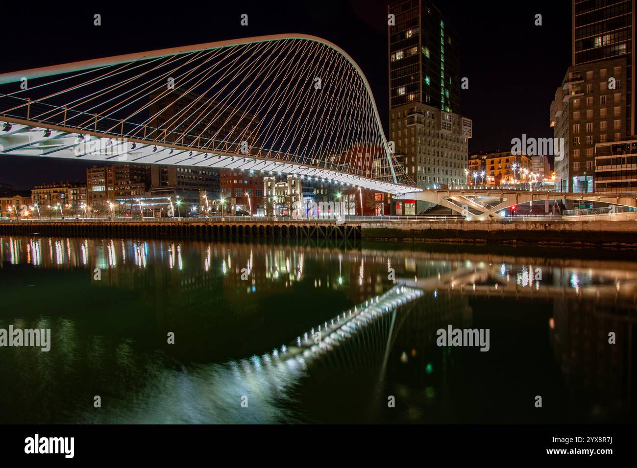 Notte al ponte Zubizuri progettato da Santiago Calatrava sul fiume Nervion a Bilbao, in Spagna, con le torri gemelle Isozaki Atea Foto Stock