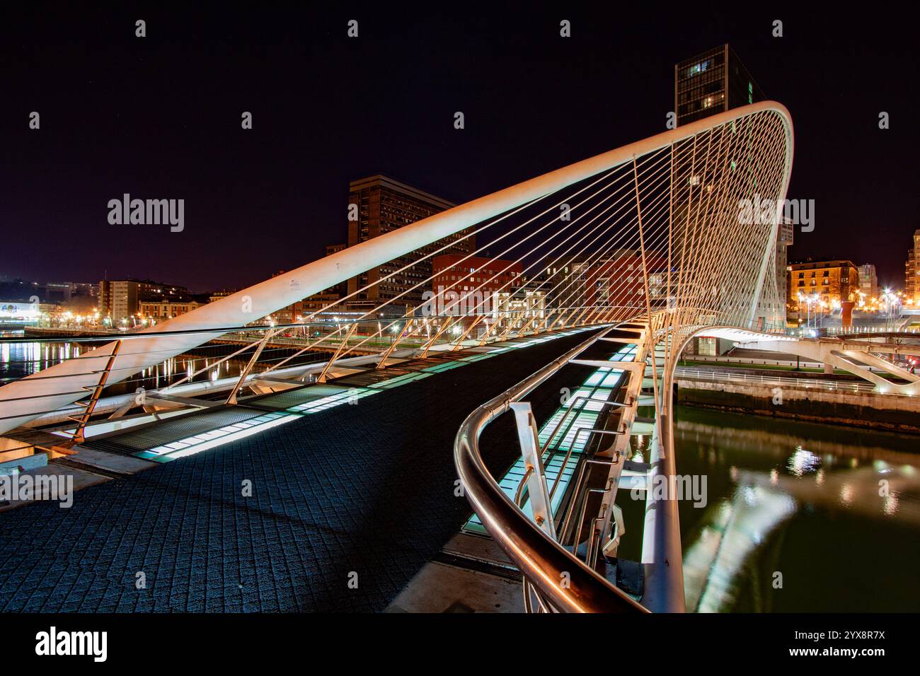 Notte al ponte Zubizuri progettato da Santiago Calatrava sul fiume Nervion a Bilbao, in Spagna, con le torri gemelle Isozaki Atea Foto Stock
