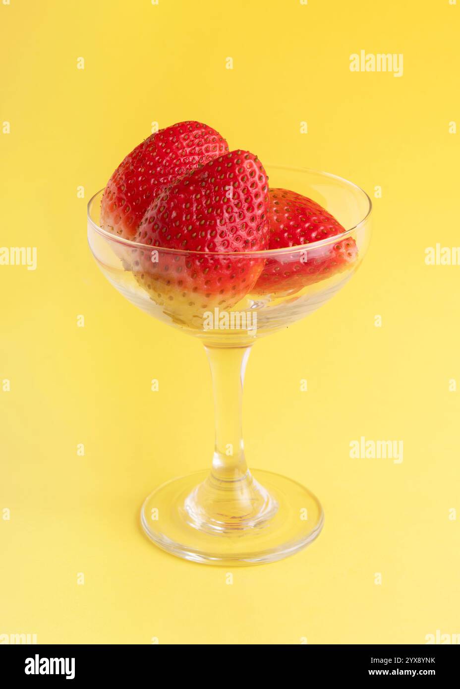 presentazione pulita di fragole fresche e vivaci in un piatto di vetro trasparente, su uno sfondo giallo audace, che mette in risalto la semplicità e la naturale bea Foto Stock