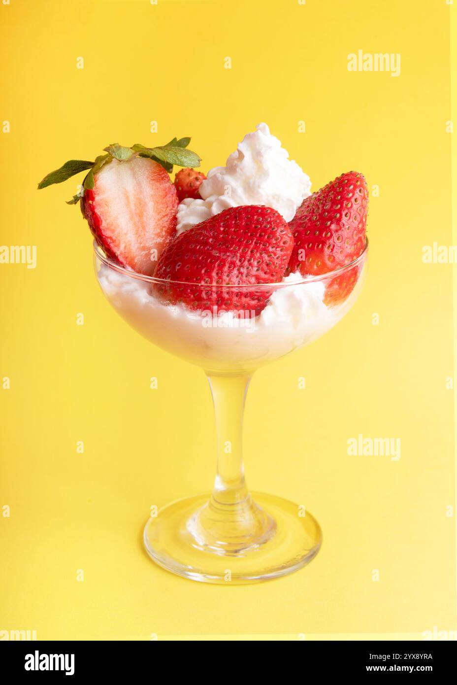 Fragole fresche, panna montata e una bacca tagliata a metà in un piatto di vetro su uno sfondo giallo soleggiato, per creare un dessert rinfrescante e appagante Foto Stock
