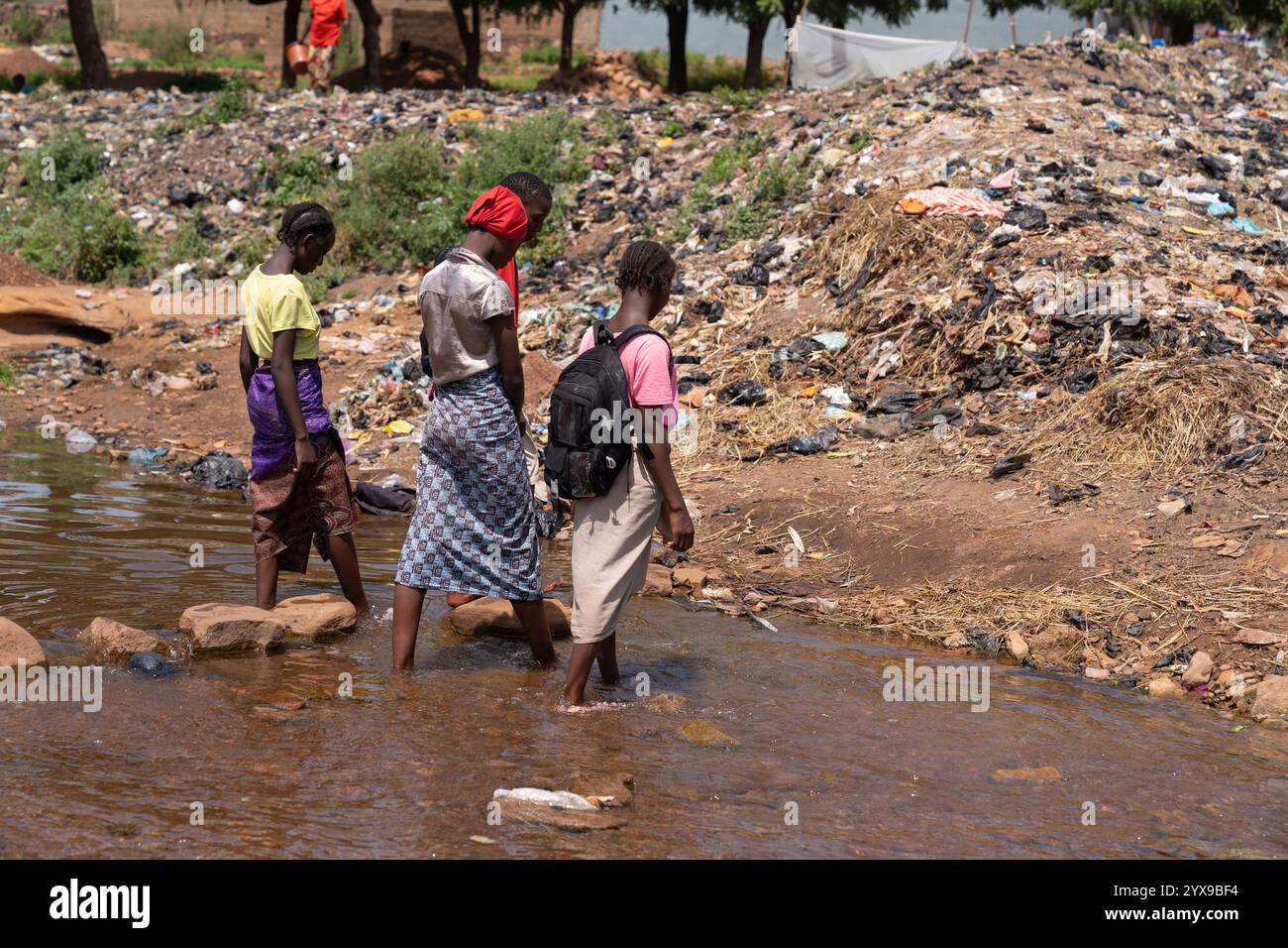 Immagine desolata di un gruppo di bambini di villaggio africani che vivono tra montagne di spazzatura a causa della mancanza di gestione dei rifiuti Foto Stock