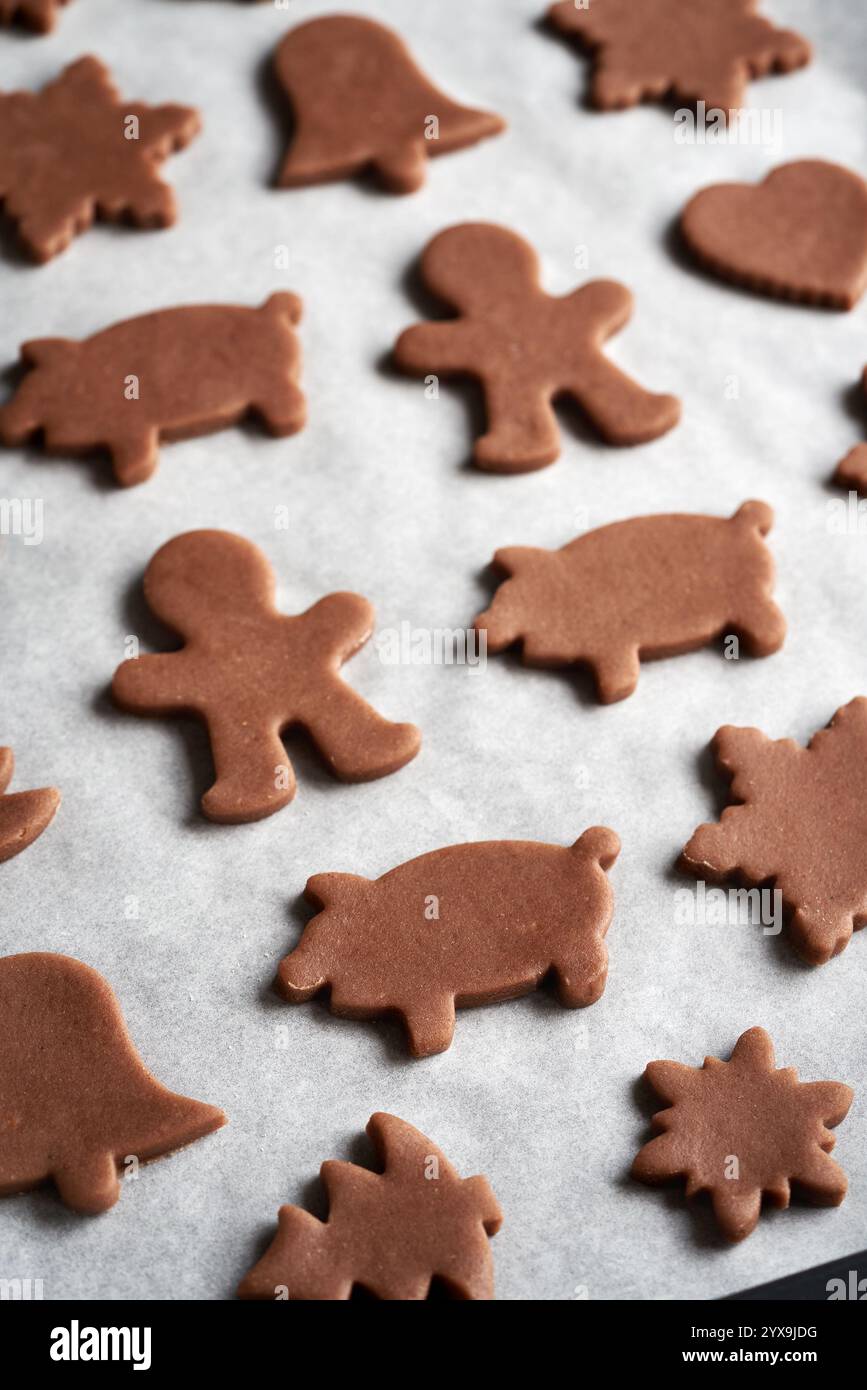 Animali e altre forme tagliate dall'impasto crudo su un foglio di carta da forno - preparazione di biscotti natalizi di pan di zenzero Foto Stock