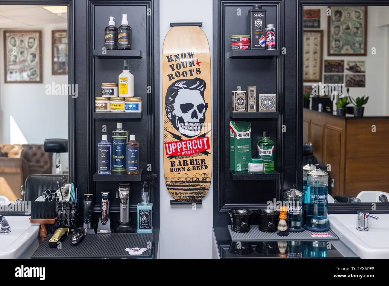 Un primo piano degli scaffali dei barbieri che espongono prodotti per la cura del corpo, strumenti per lo styling dei capelli e un audace arredamento da skateboard con il marchio "Uppercut Deluxe". Foto Stock
