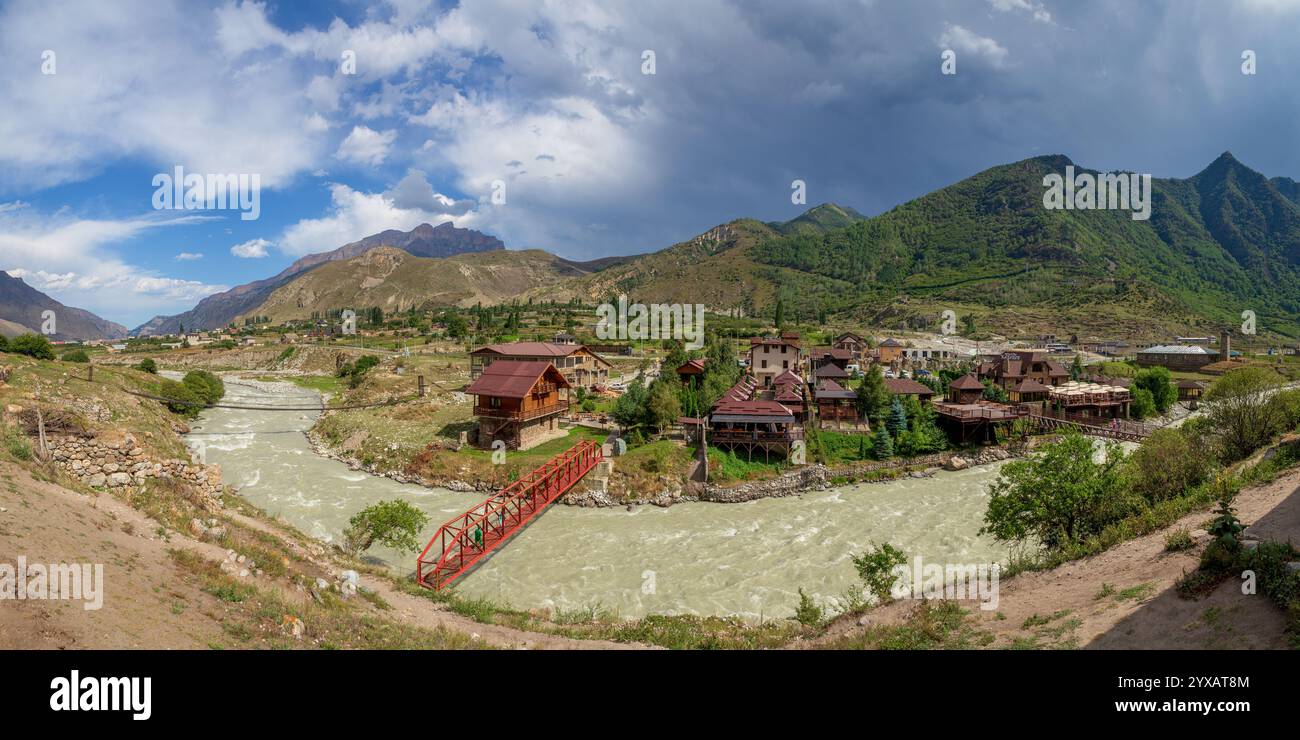 Paesaggio panoramico di un villaggio sulle montagne del Caucaso con un fiume in primo piano Foto Stock