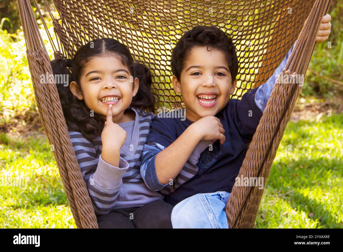 Sorridenti gemelli seduti in un'amaca in giardino, Florida, Stati Uniti Foto Stock