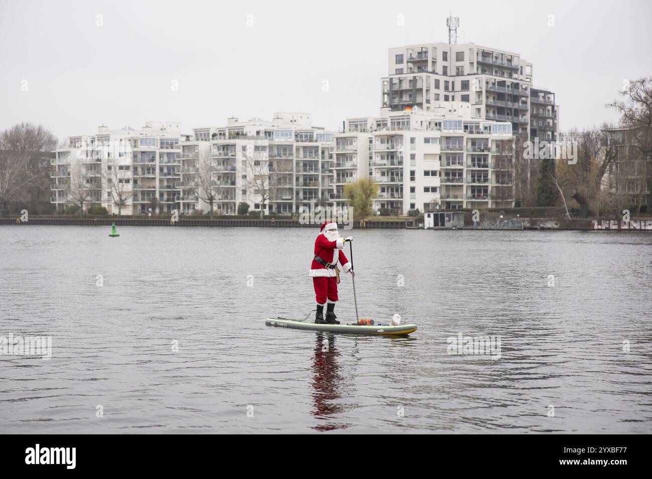 Un appassionato di sport acquatici vestito da Babbo Natale cavalca sup sulla Sprea a Berlino il 14 dicembre 2024 Foto Stock