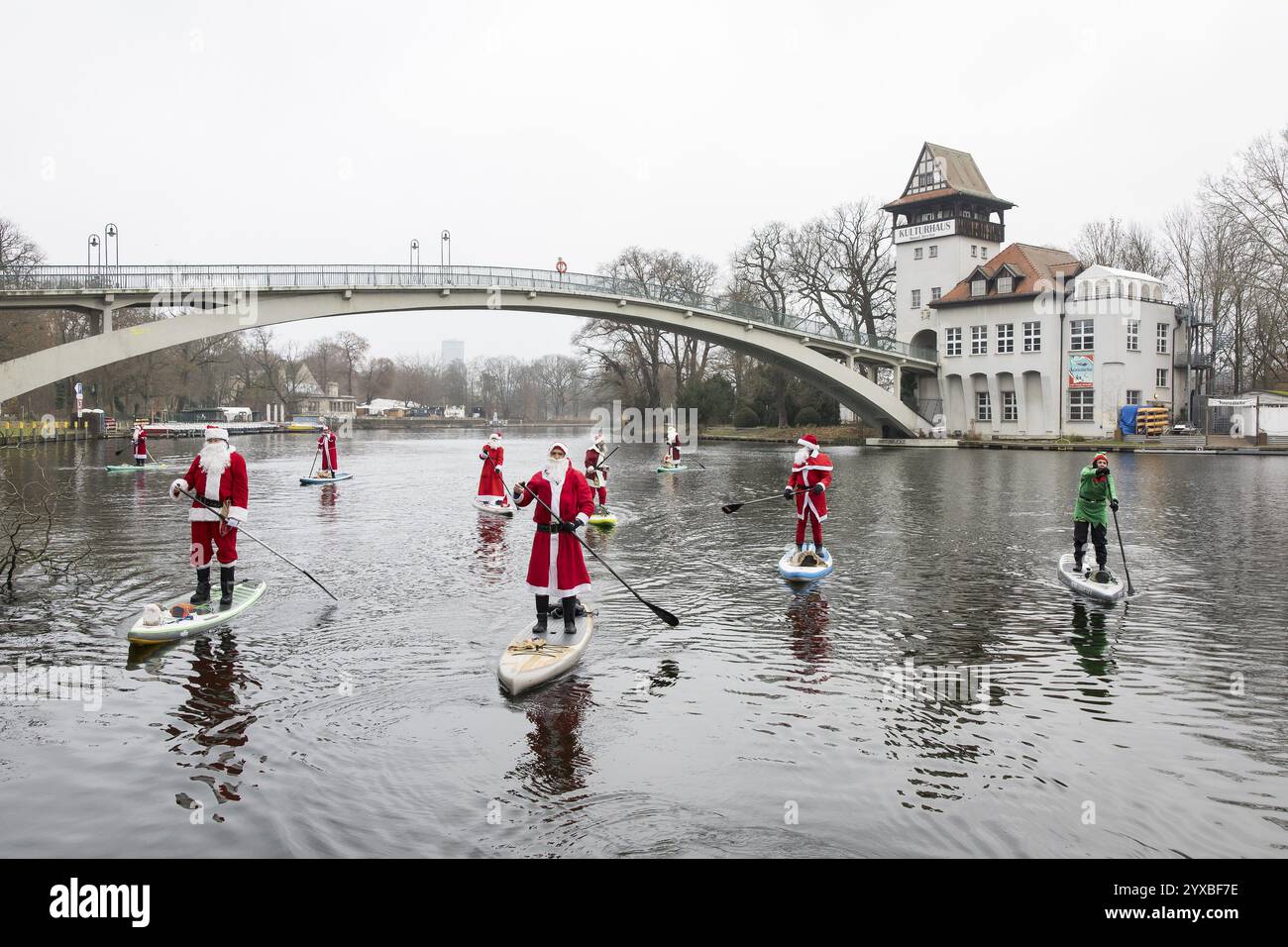 Gli appassionati di sport acquatici, vestiti da Santas, cavalcano SUP sulla Sprea di fronte all'Insel der Jugend di Berlino il 14 dicembre 2024 Foto Stock