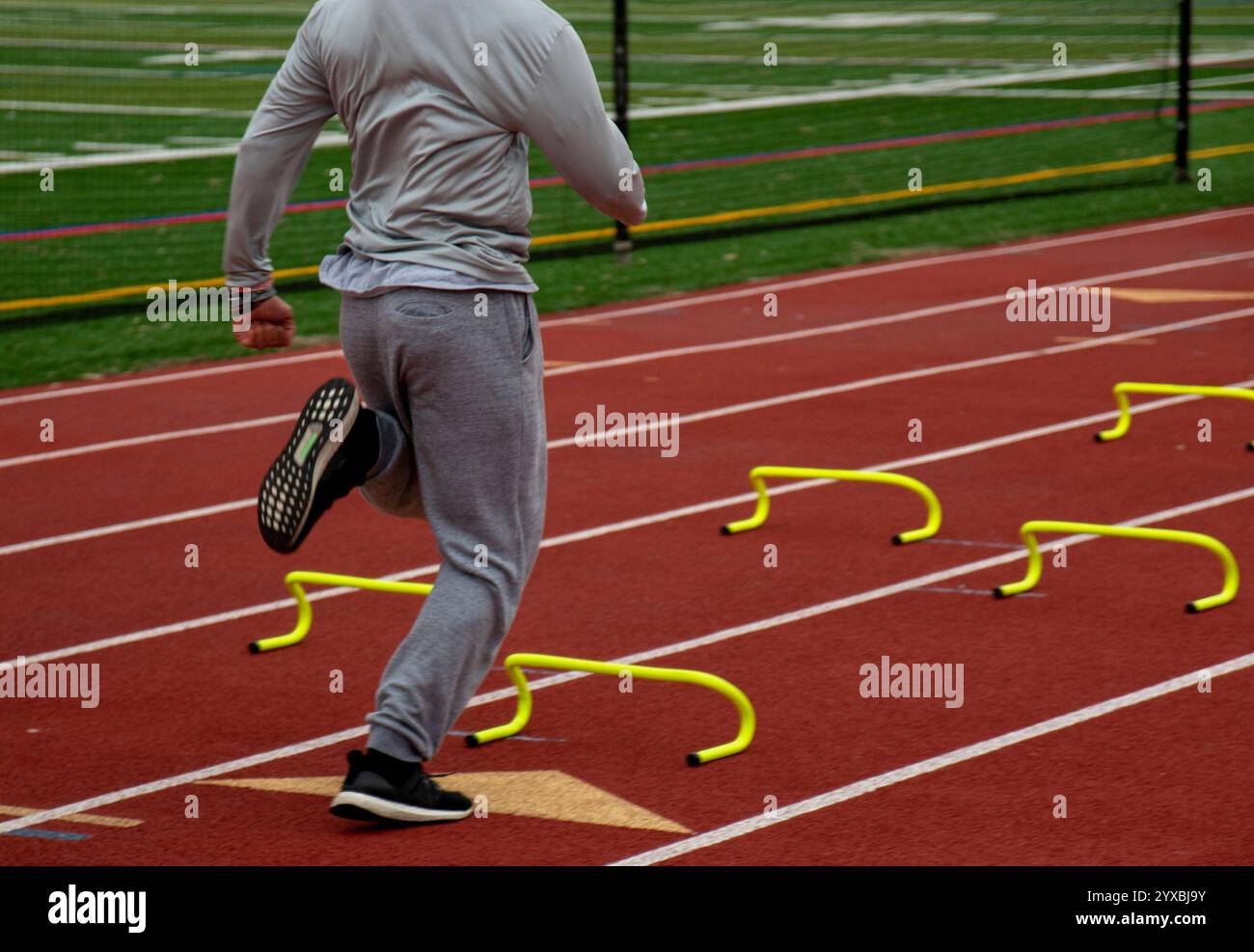 L'atleta pratica usando ostacoli su una pista da corsa rossa in una struttura sportiva all'aperto. Foto Stock