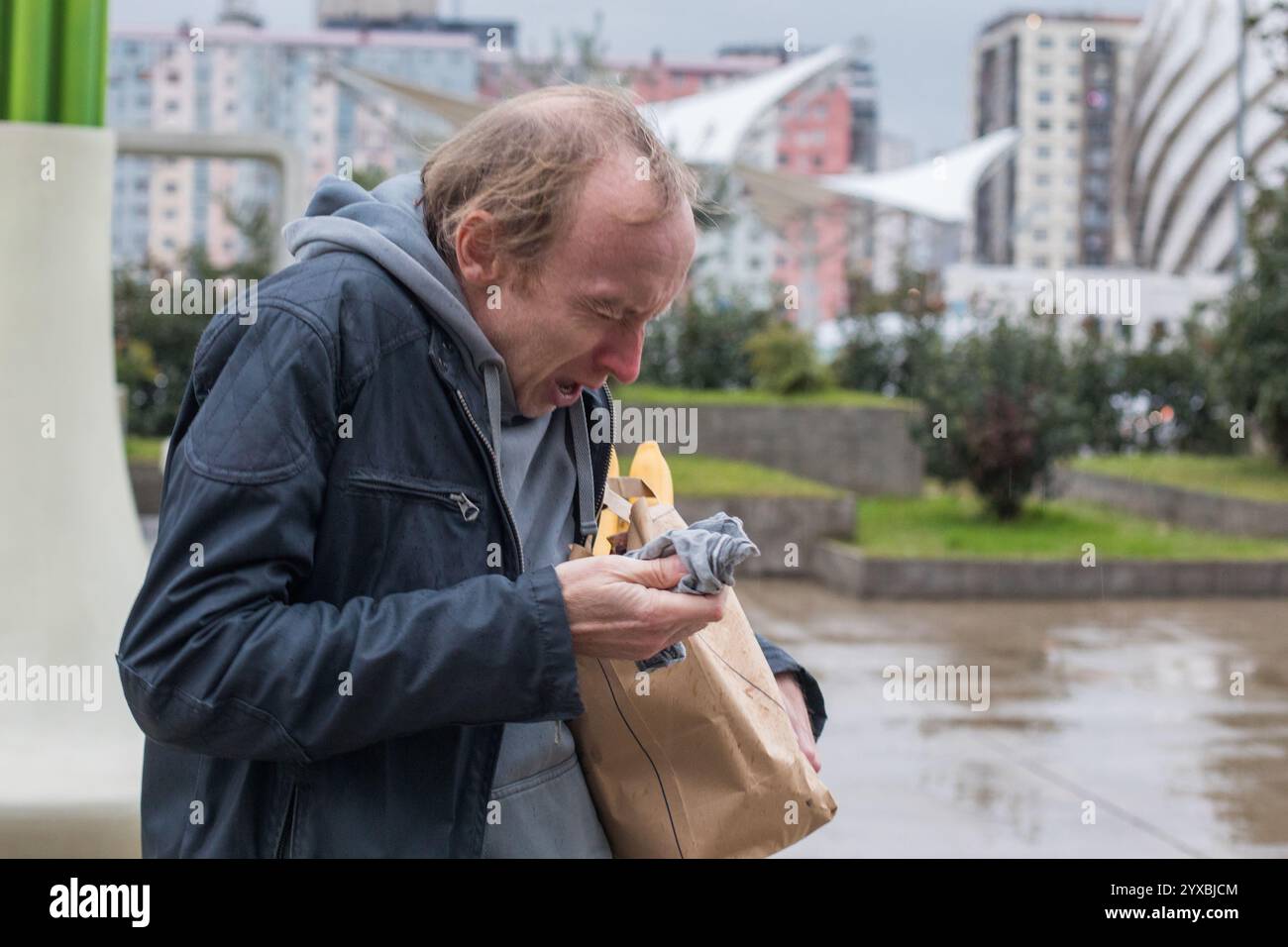Starnuto uomo con influenza stagionale sta camminando sulla strada della città e tosse nei tessuti. Foto Stock