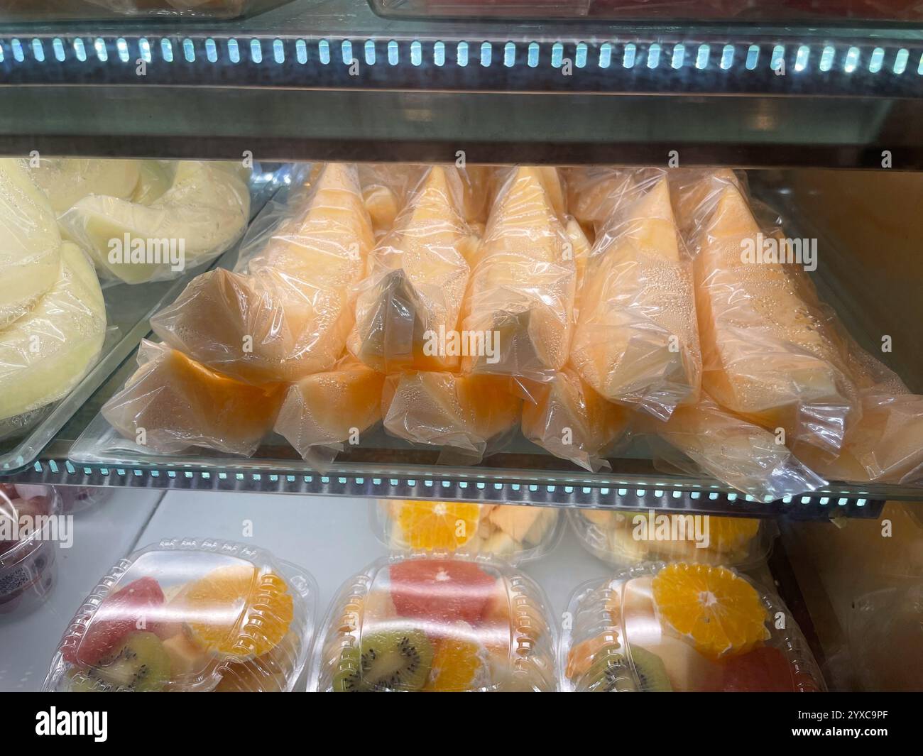 Fette di melone ripiene avvolte in plastica con contenitori di frutta confezionati sotto, compresi arance, kiwi e anguria. Aeroporto Changi di Singapore Foto Stock
