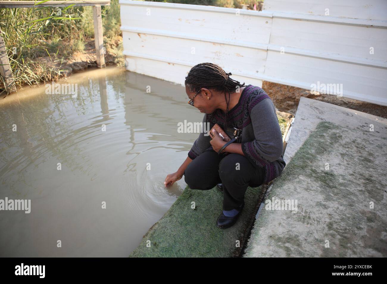 Donna ghanese, pellegrina cristiana evangelica mette la mano nel fiume Giordano a Qasr El Yahud, dove Giovanni Battista battezzò Gesù Cristo Foto Stock