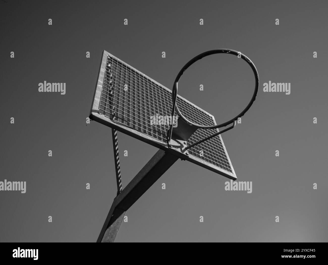 Vista ravvicinata di un canestro da basket minimalista con una sponda posteriore in mesh metallica sullo sfondo di un cielo limpido in bianco e nero Foto Stock