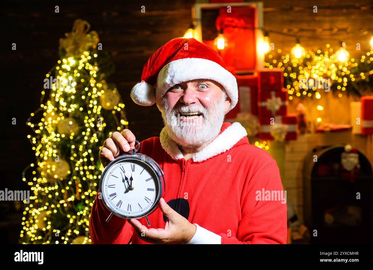 Buon Babbo Natale in attesa dell'orologio che mostra cinque minuti a mezzanotte. Conto alla rovescia per l'anno nuovo. Uomo barbuto in abiti di Babbo Natale con l'orologio di Capodanno. Babbo Natale con Foto Stock