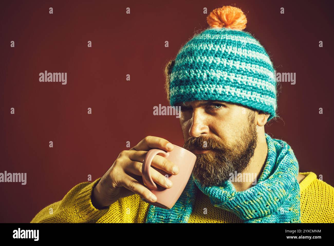 L'ora del caffè. Uomo barbuto serio con maglione a maglia, cappello e sciarpa bevendo una tazza di tè o caffè. Bel ragazzo con barba e baffi in abbigliamento casual Foto Stock