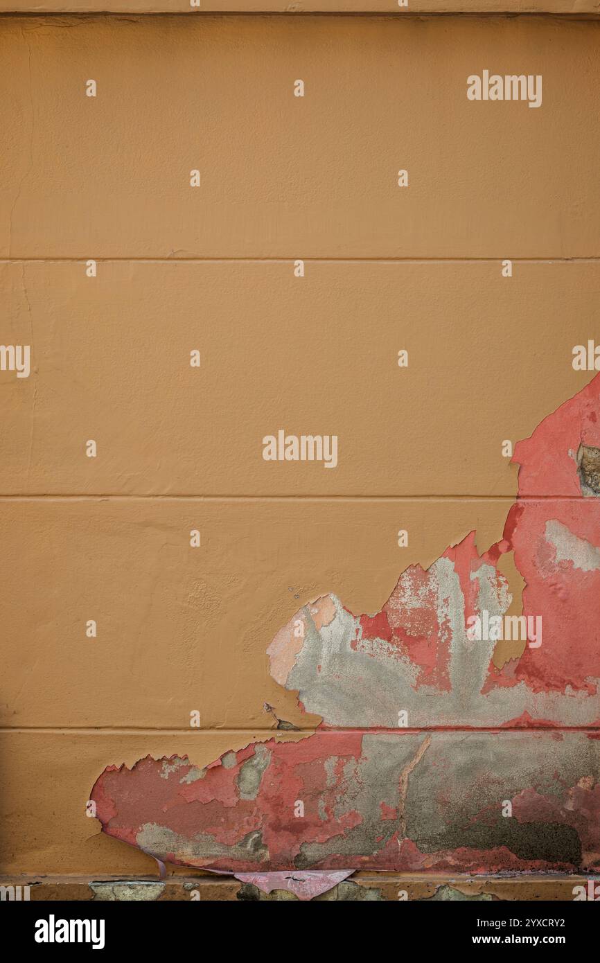 Vista frontale di una parete dipinta di arancione. La vernice viene parzialmente rimossa rivelando vernice rosa e cemento grezzo. Sfondo strutturato full frame astratto. Foto Stock