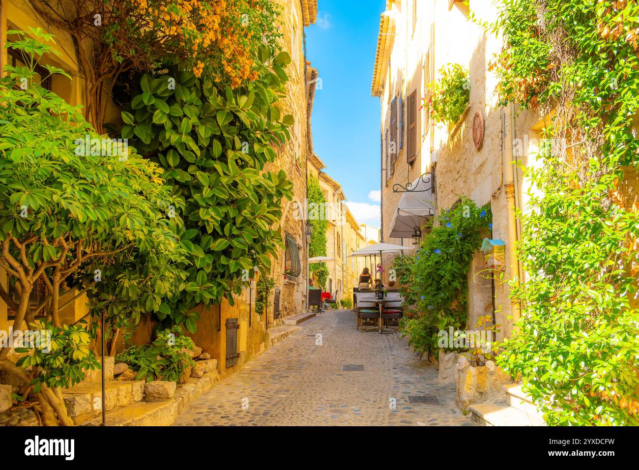 Uno stretto vicolo acciottolato con negozi e caffetterie sul marciapiede nel centro storico medievale del villaggio collinare di Saint Paul de Vence, Francia. Foto Stock