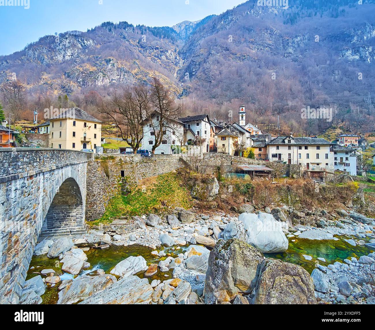 L'antico ponte in pietra che attraversa il fiume Maggia e il medioevale borgo di Prato Sornico contro le Alpi rocciose, la Val Lavizzara, Vallemaggia, Ticin Foto Stock