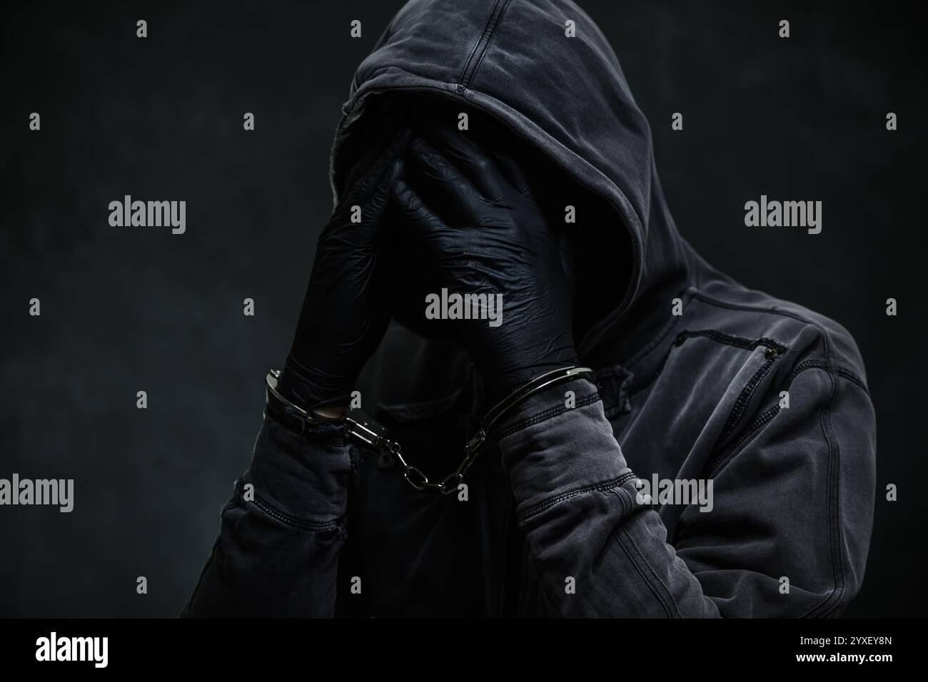 Manette criminali indossando felpa con cappuccio e coprendo il viso con le mani, messa a fuoco selettiva Foto Stock