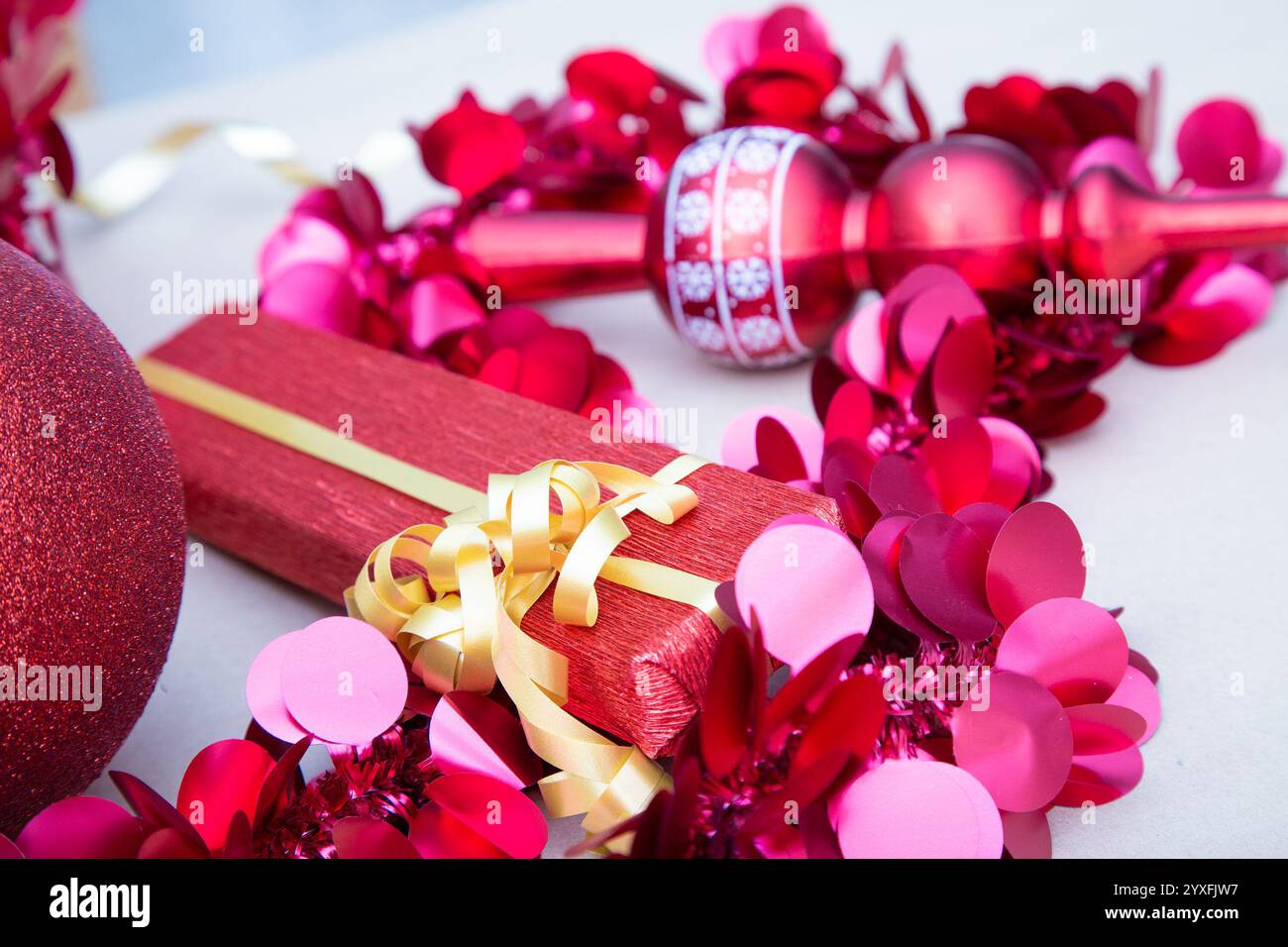 Un regalo rosso con un fiocco d'oro è circondato da decorazioni rosa Foto Stock