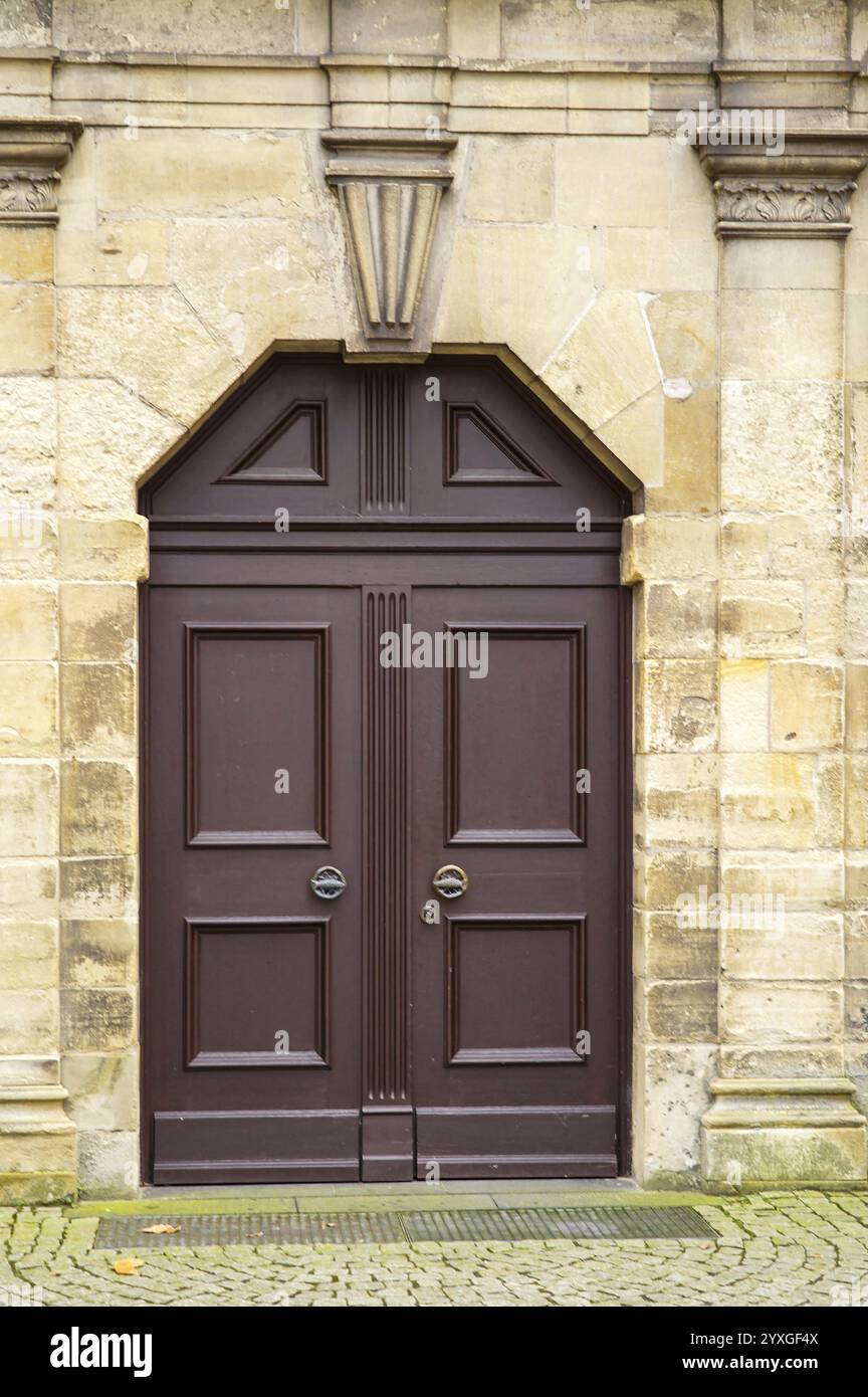 Porta doppia marrone collocata all'interno di una porta ad arco in pietra, che aggiunge un tocco di eleganza alla facciata dell'edificio Foto Stock